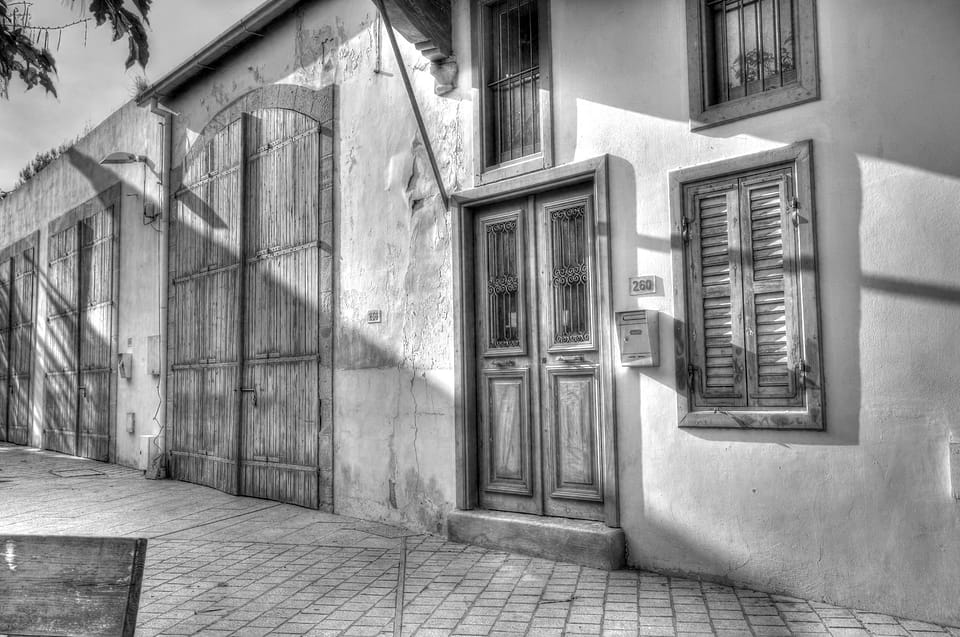 Paredes caiadas com portas e portadas de madeira, sombras no chão de pedra