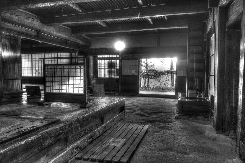 Interior de uma casa de madeira, com luz a entrar pela porta do fundo