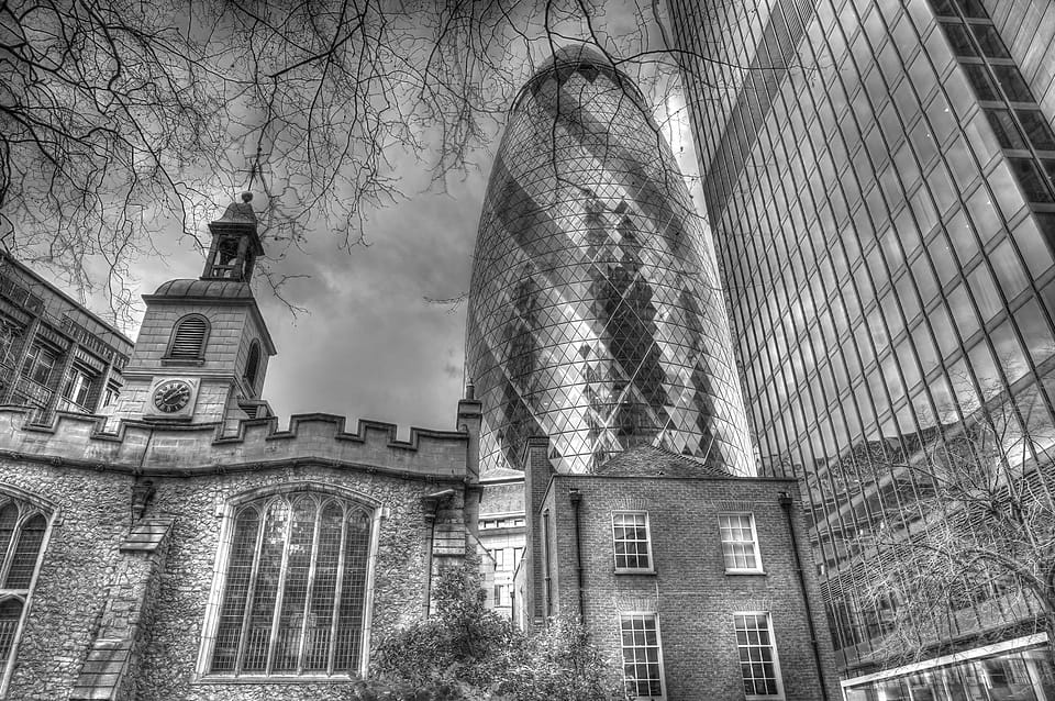 Igreja de tijolo com relógio diante da torre envidraçada do Gherkin