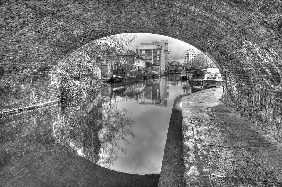 Canal visto através do arco de um túnel, com barcos atracados e reflexos na água