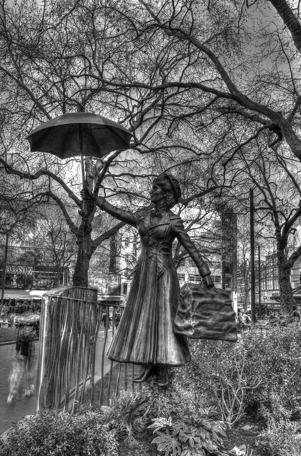 Estátua de bronze de uma mulher com um guarda-chuva erguido, entre árvores